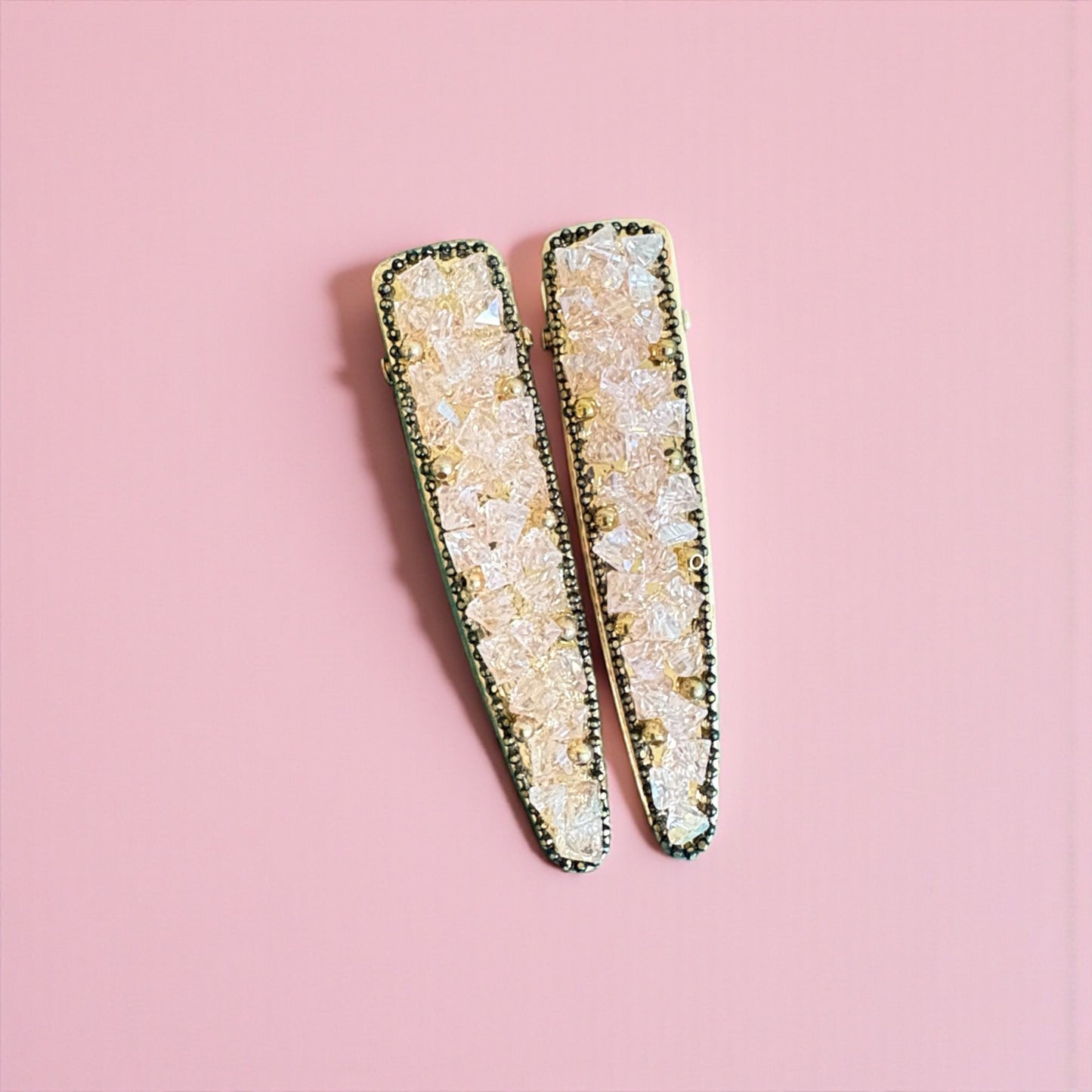 Decorative hair clips with a textured design on a pink background