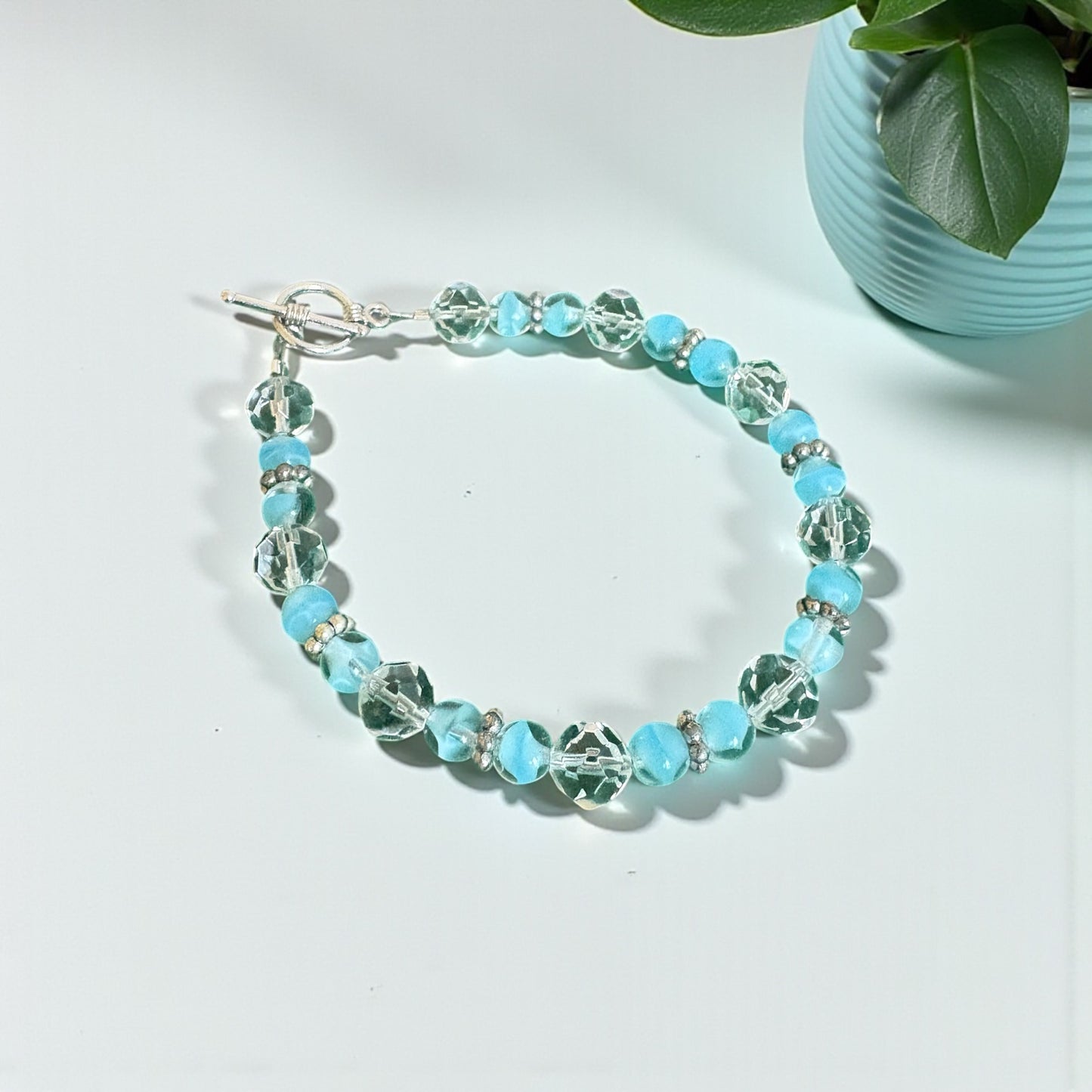 Turquoise beaded bracelet on a light surface with a plant in the background