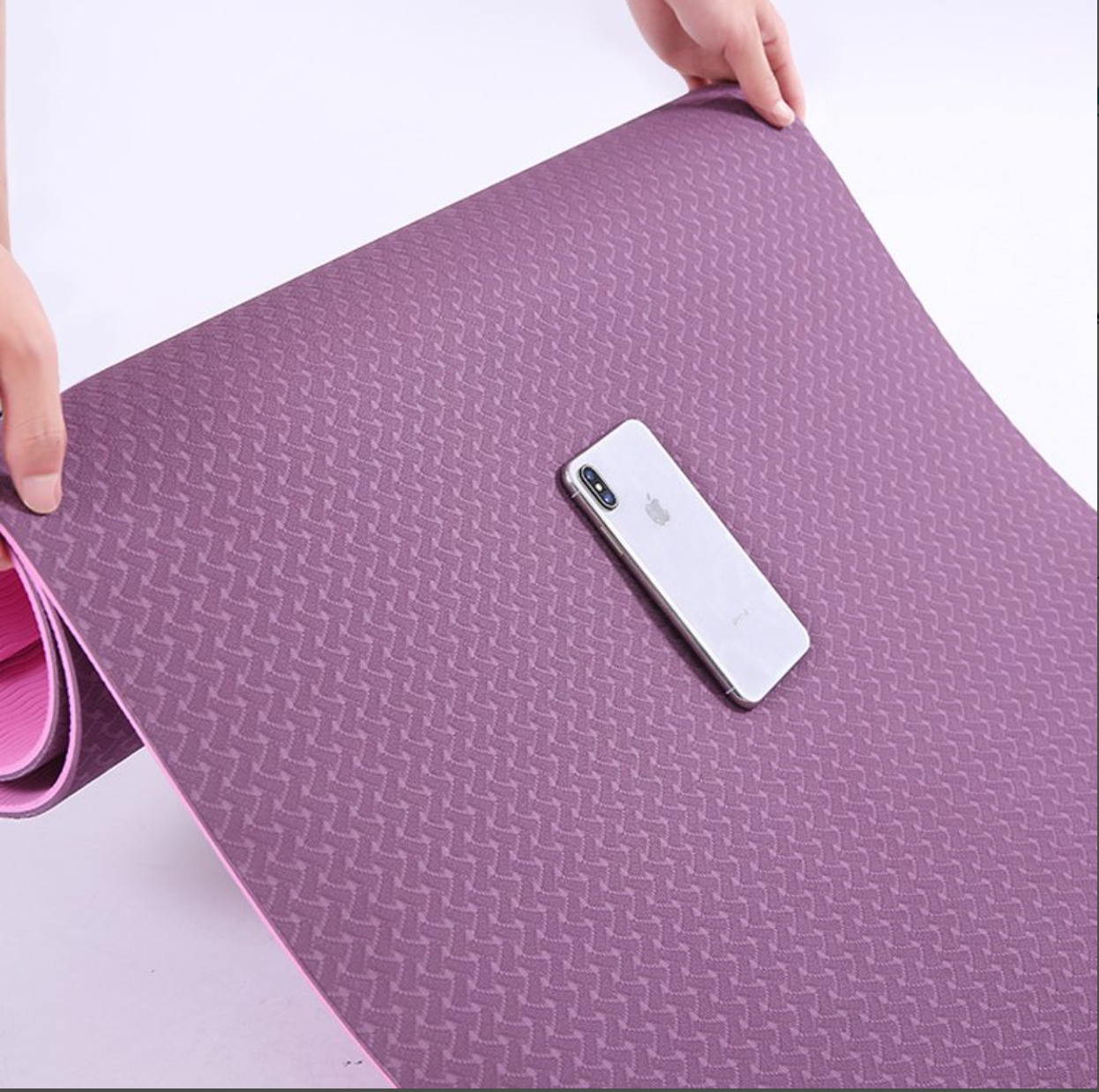 Purple yoga mat with a phone on top, held by hands against a white background