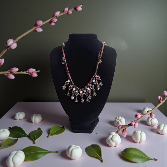Necklace on a black mannequin bust with decorative branches and white fruits on a light pink surface.