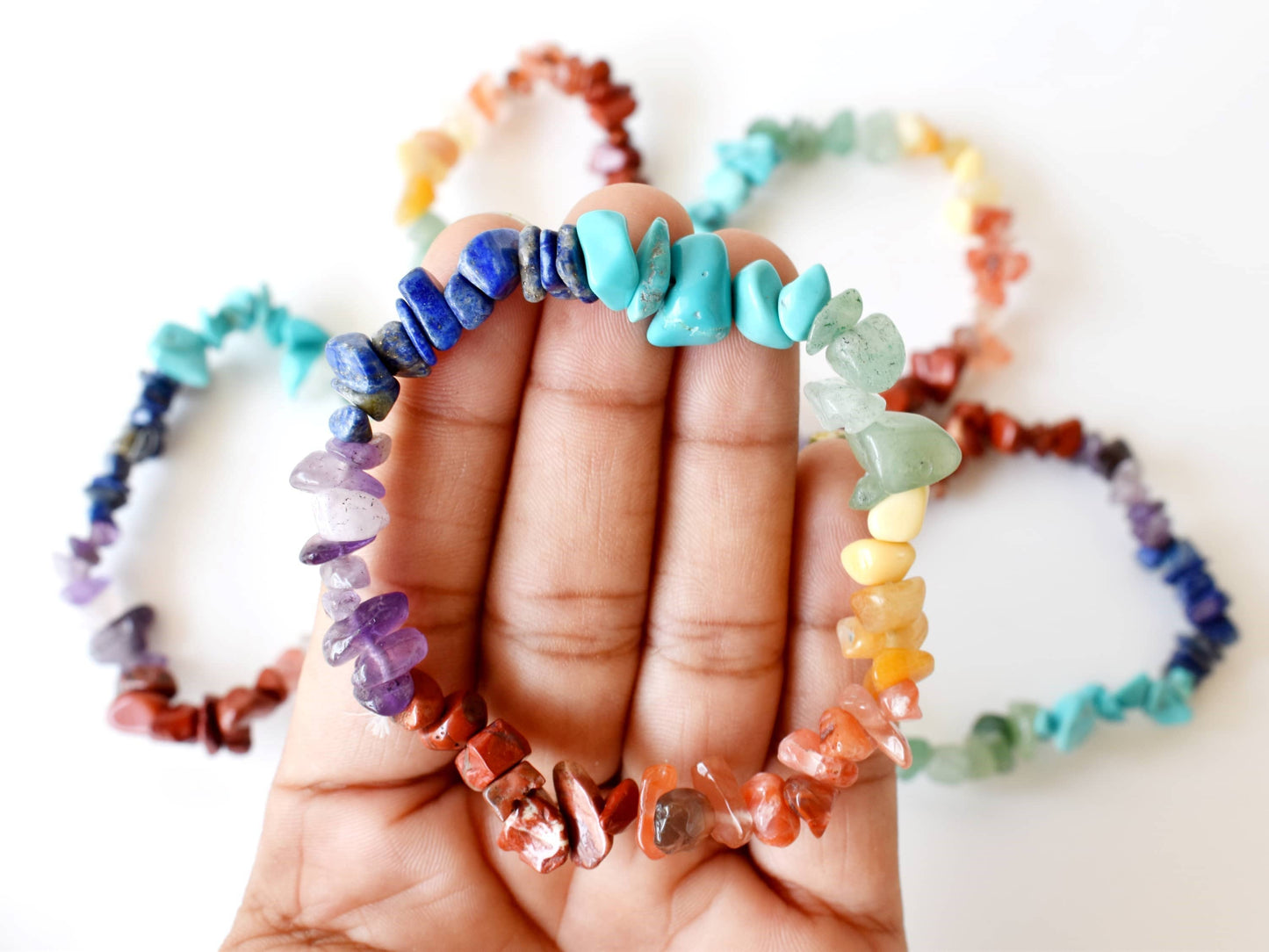 Hand holding a colorful beaded bracelet with more bracelets in the background on a white surface