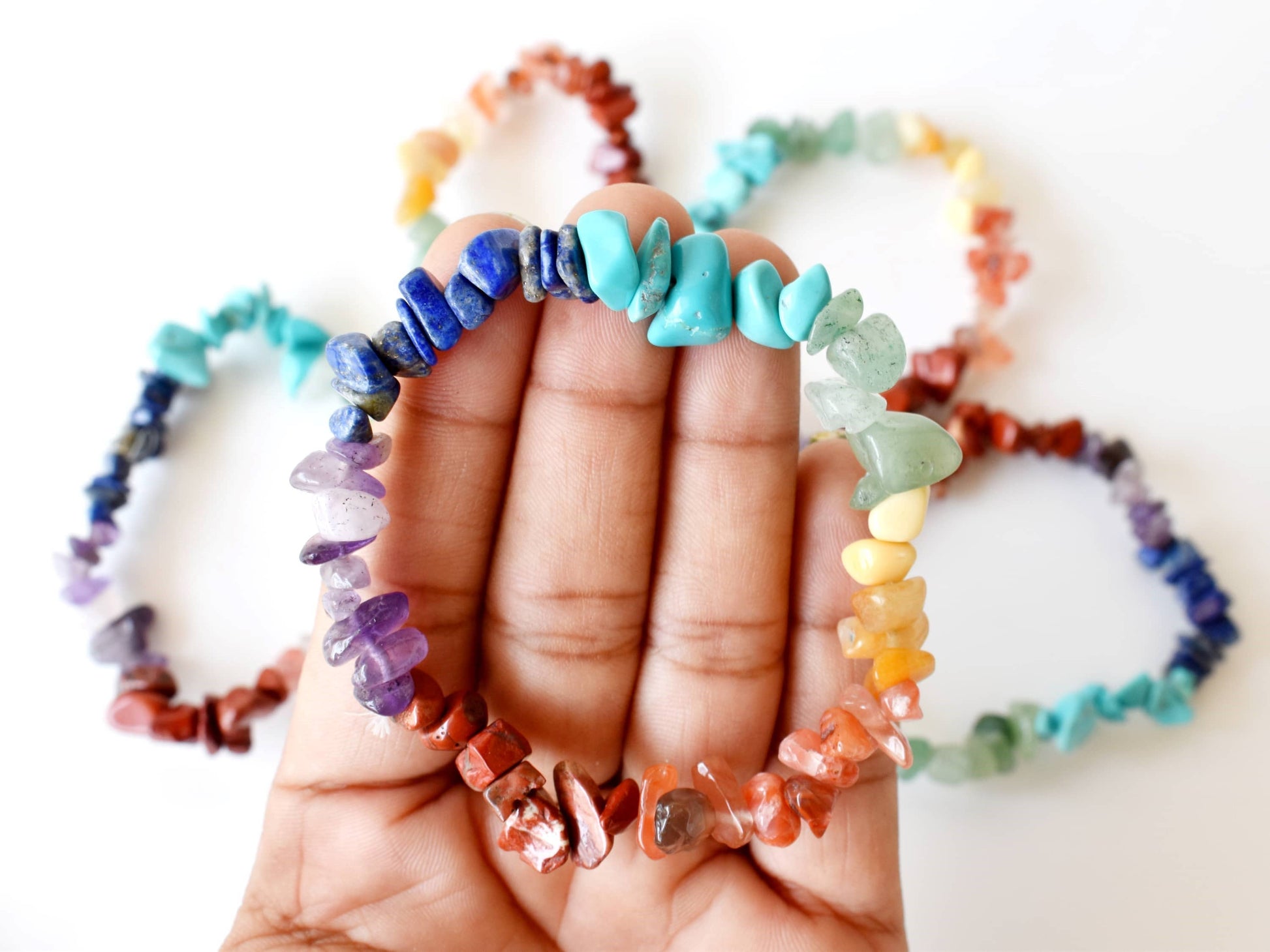 Hand holding a colorful beaded bracelet with more bracelets in the background on a white surface