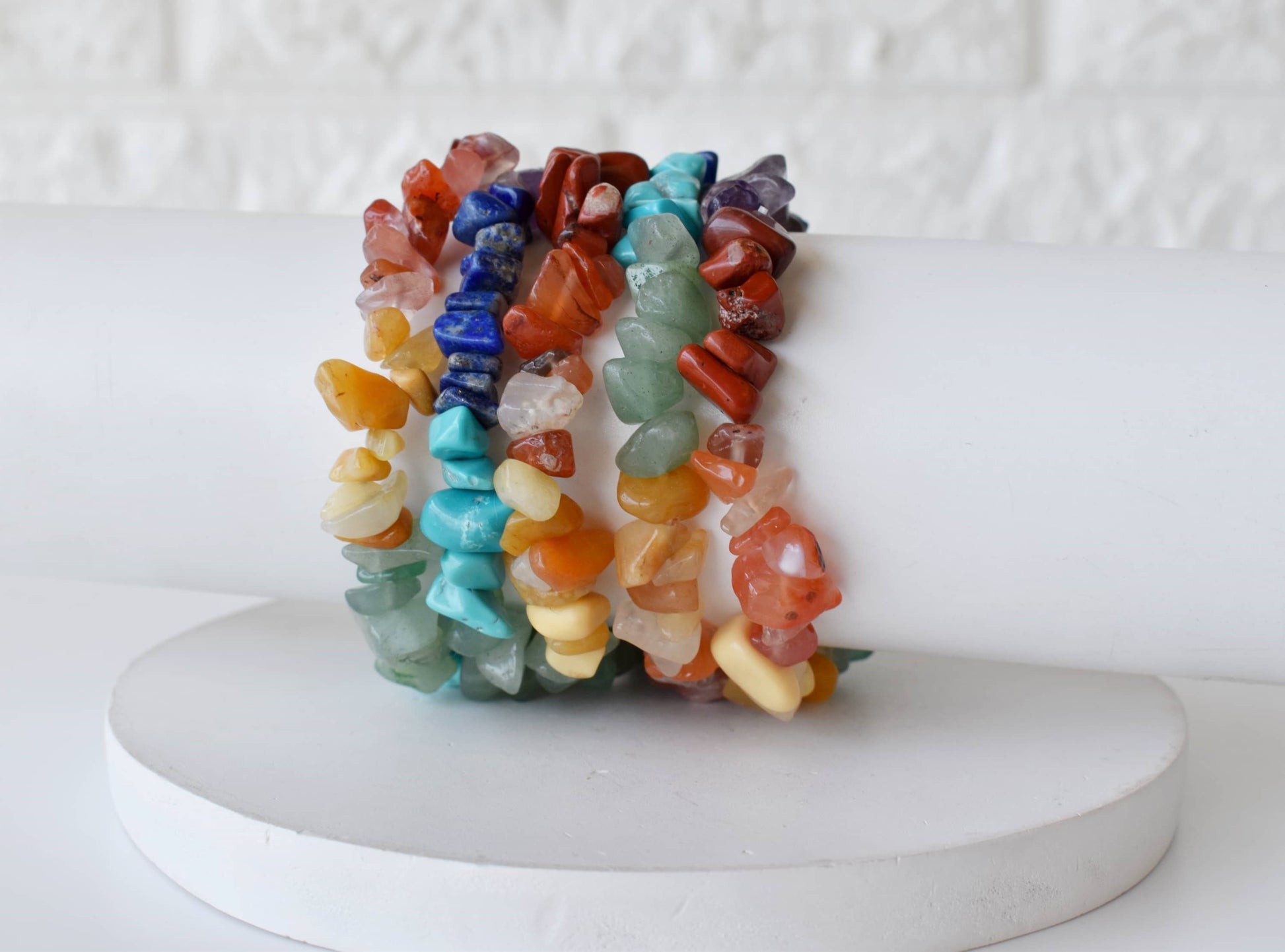 Set of colorful stone bracelets on a white pedestal with a white background