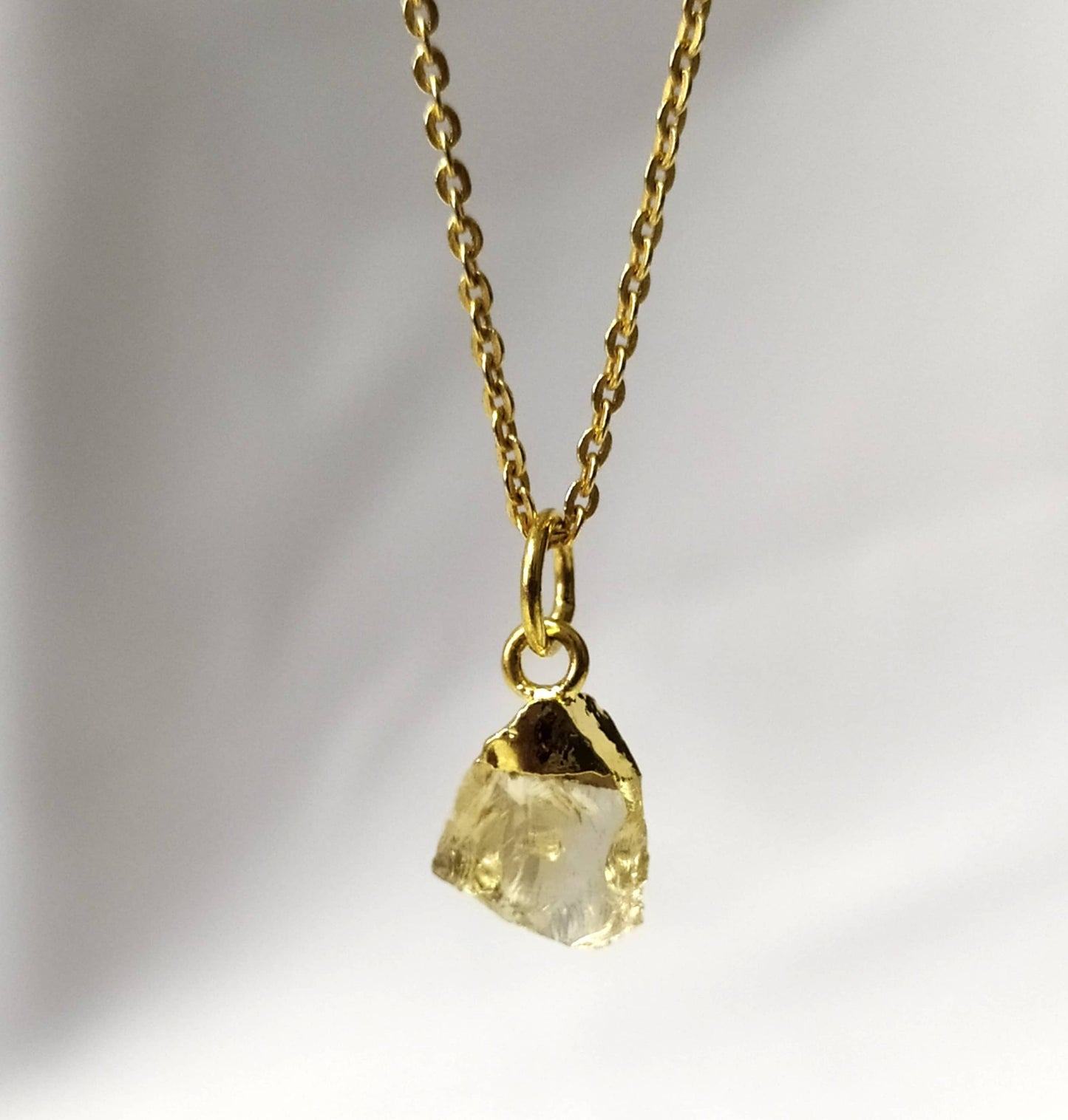 Gold necklace with a clear crystal pendant on a gradient background