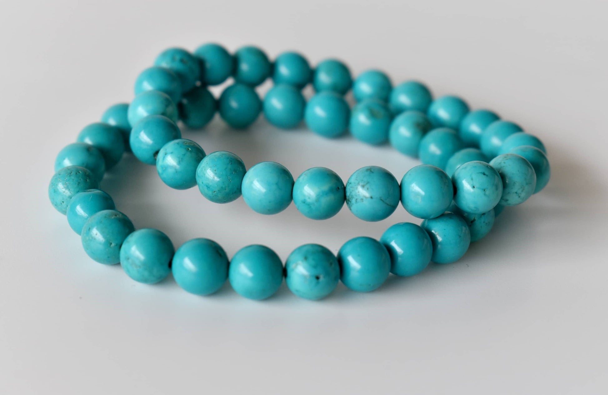 Two turquoise beaded bracelets on a light gray background