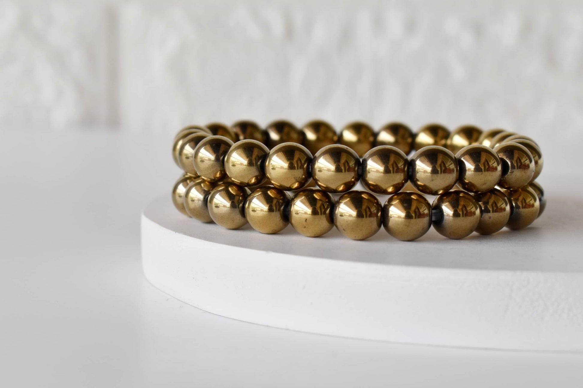 Gold beaded bracelet on a white stand with a white background