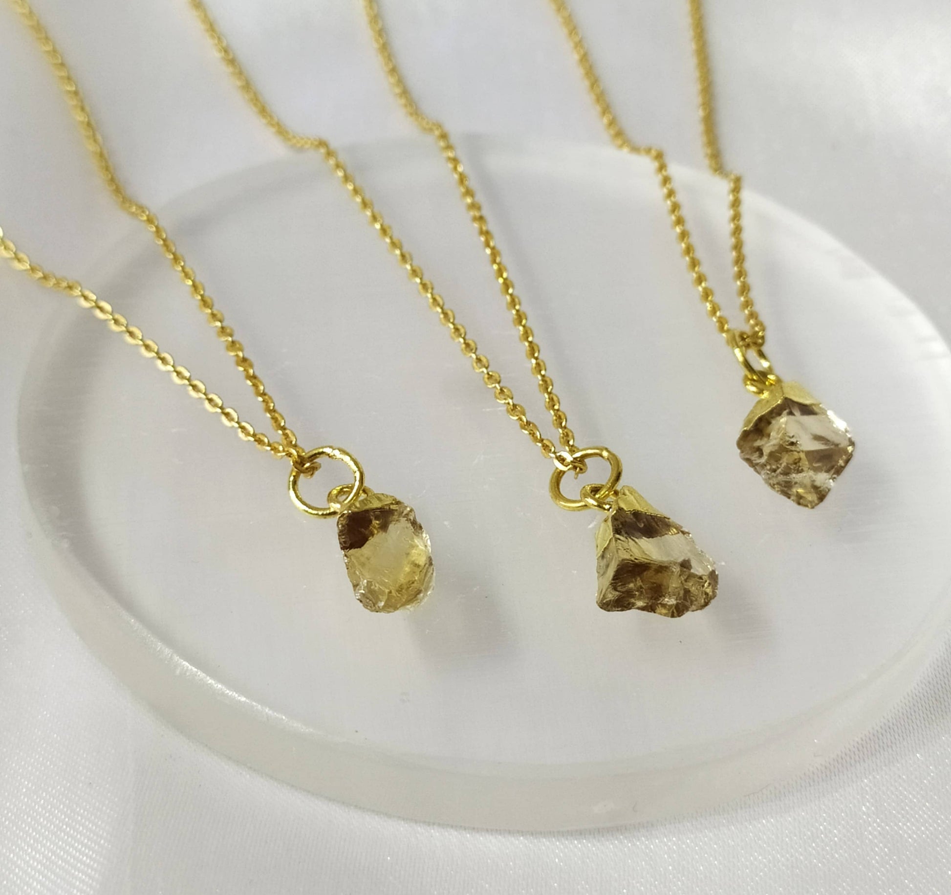 Three gold necklaces with crystal pendants on a clear plate