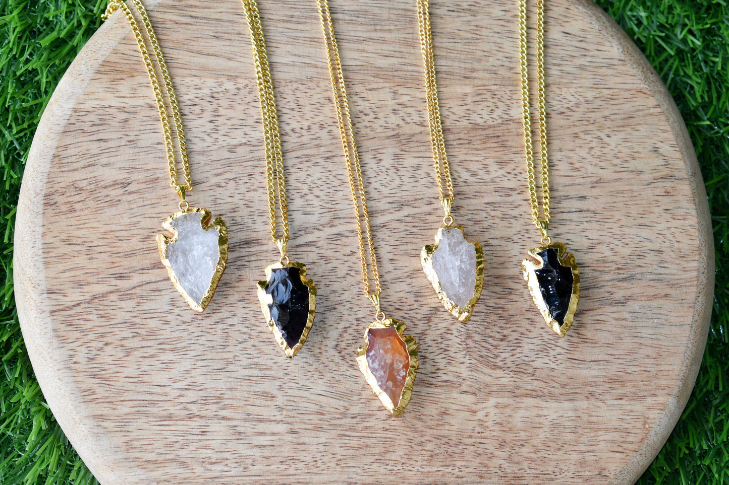Five gold necklaces with various stone pendants on a wooden board.
