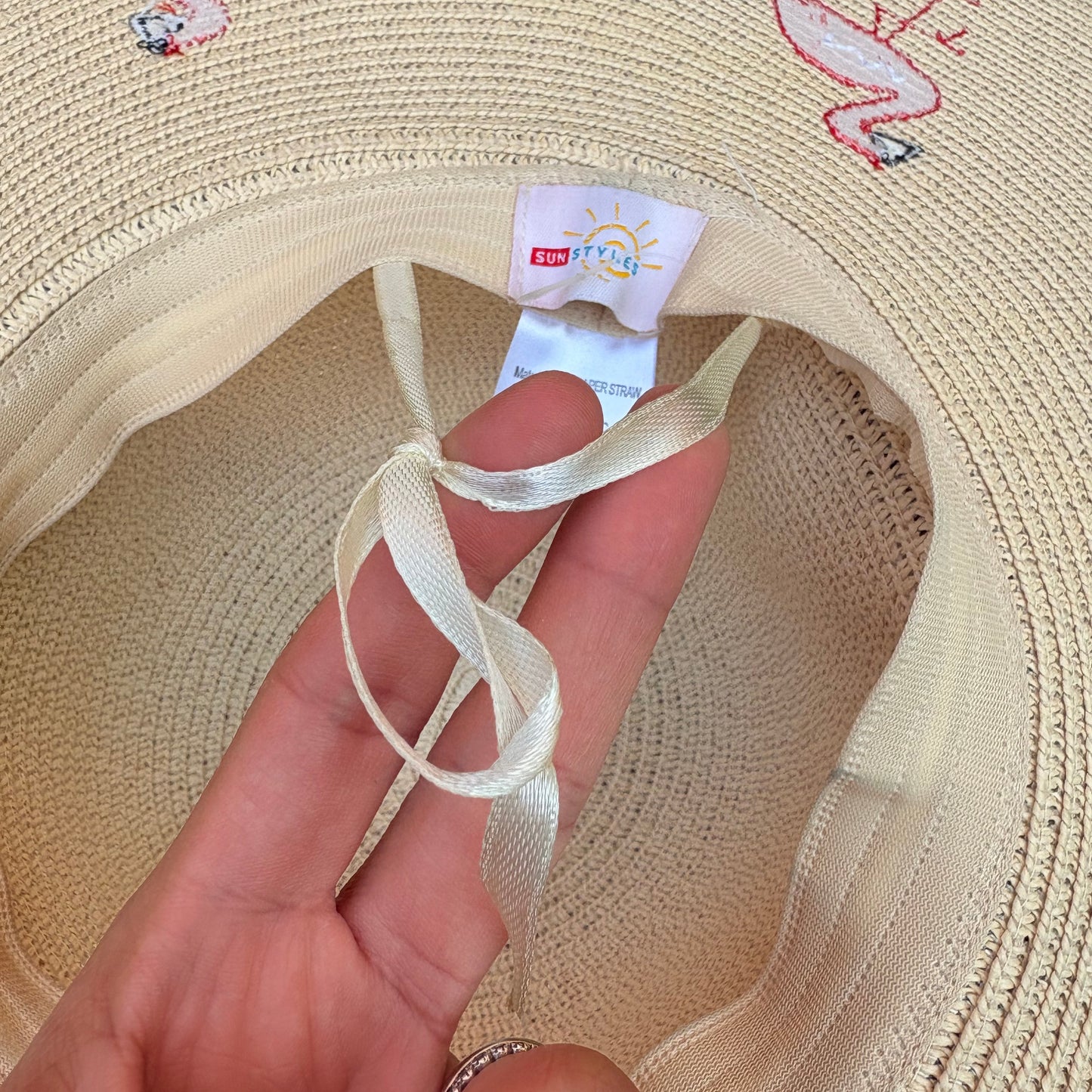 Beige sun hat with pink flamingo designs on a grass background
