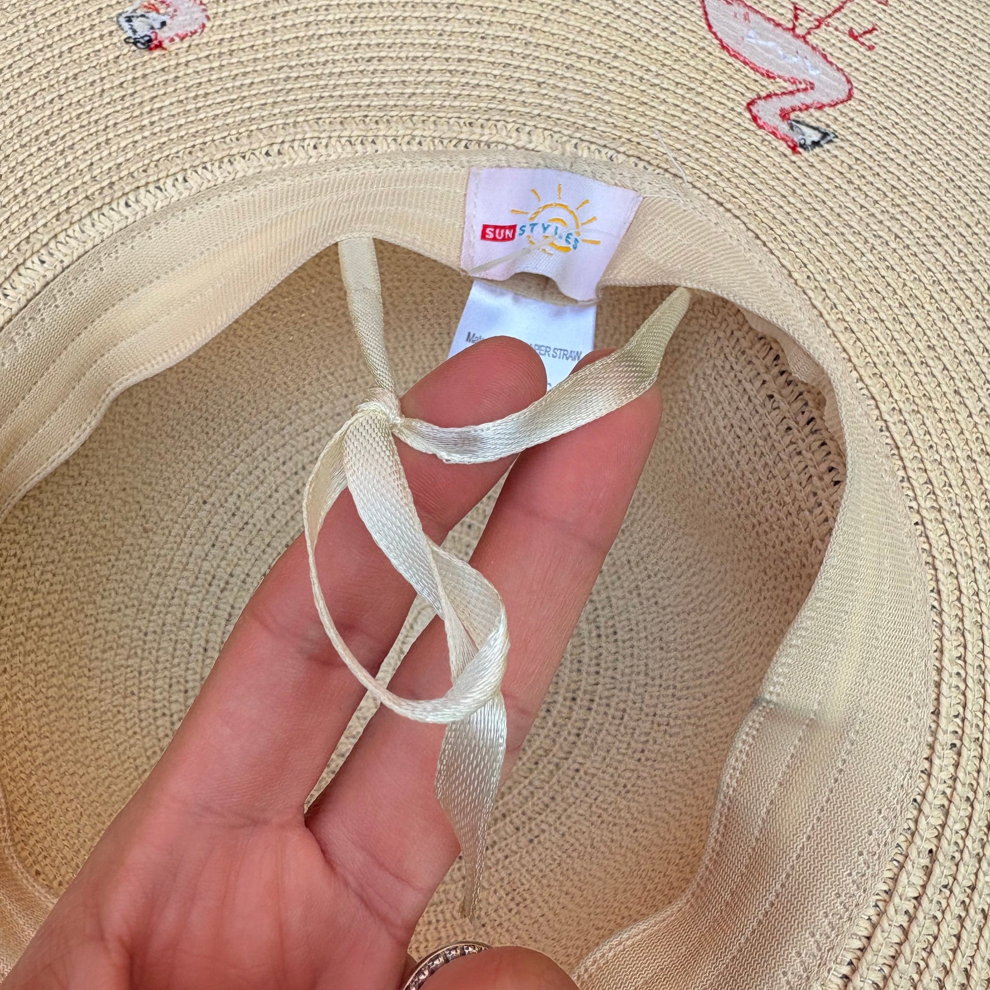 Beige sun hat with pink flamingo designs on a grass background