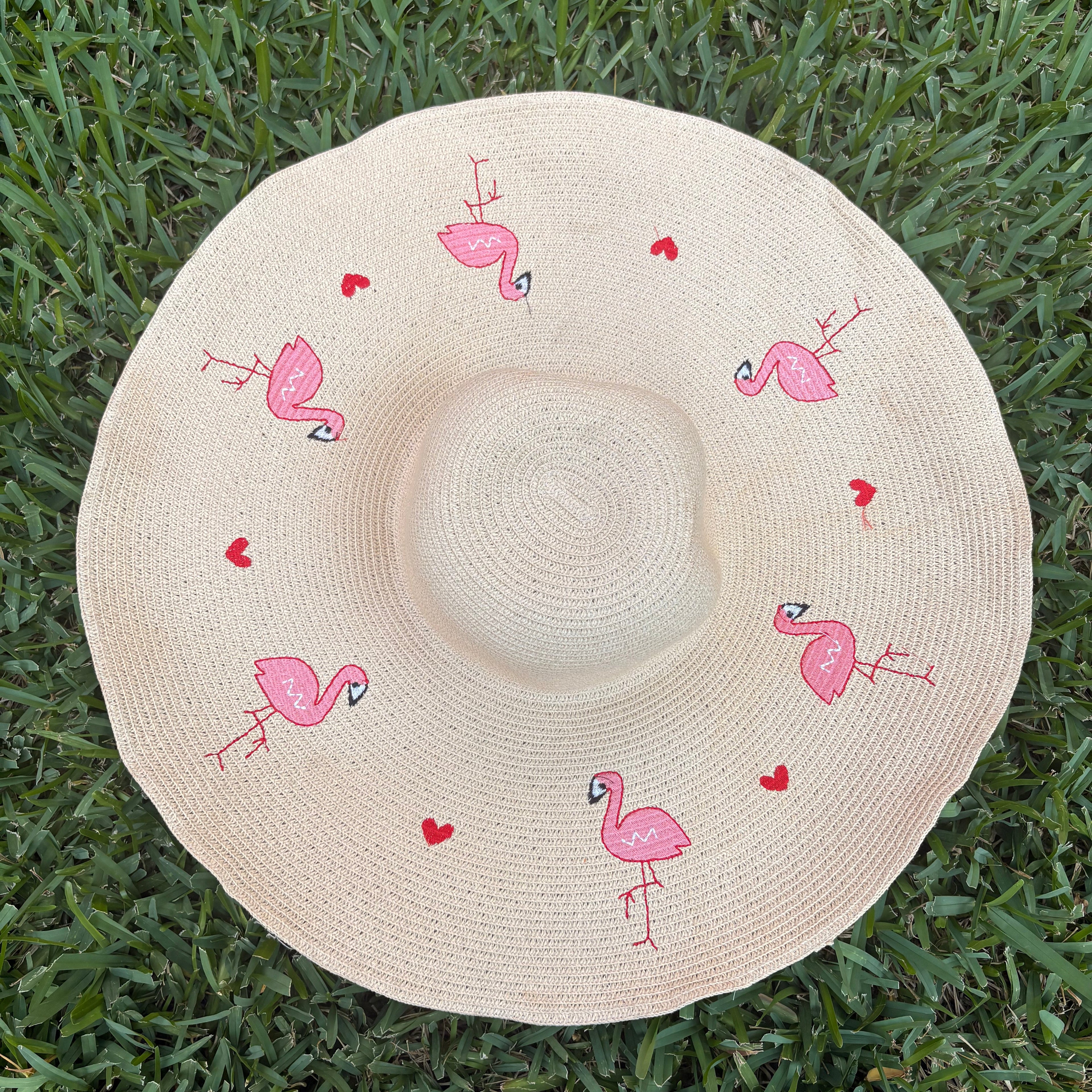 Beige sun hat with pink flamingo designs on a grass background