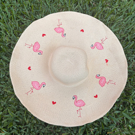 Beige sun hat with pink flamingo designs on a grass background