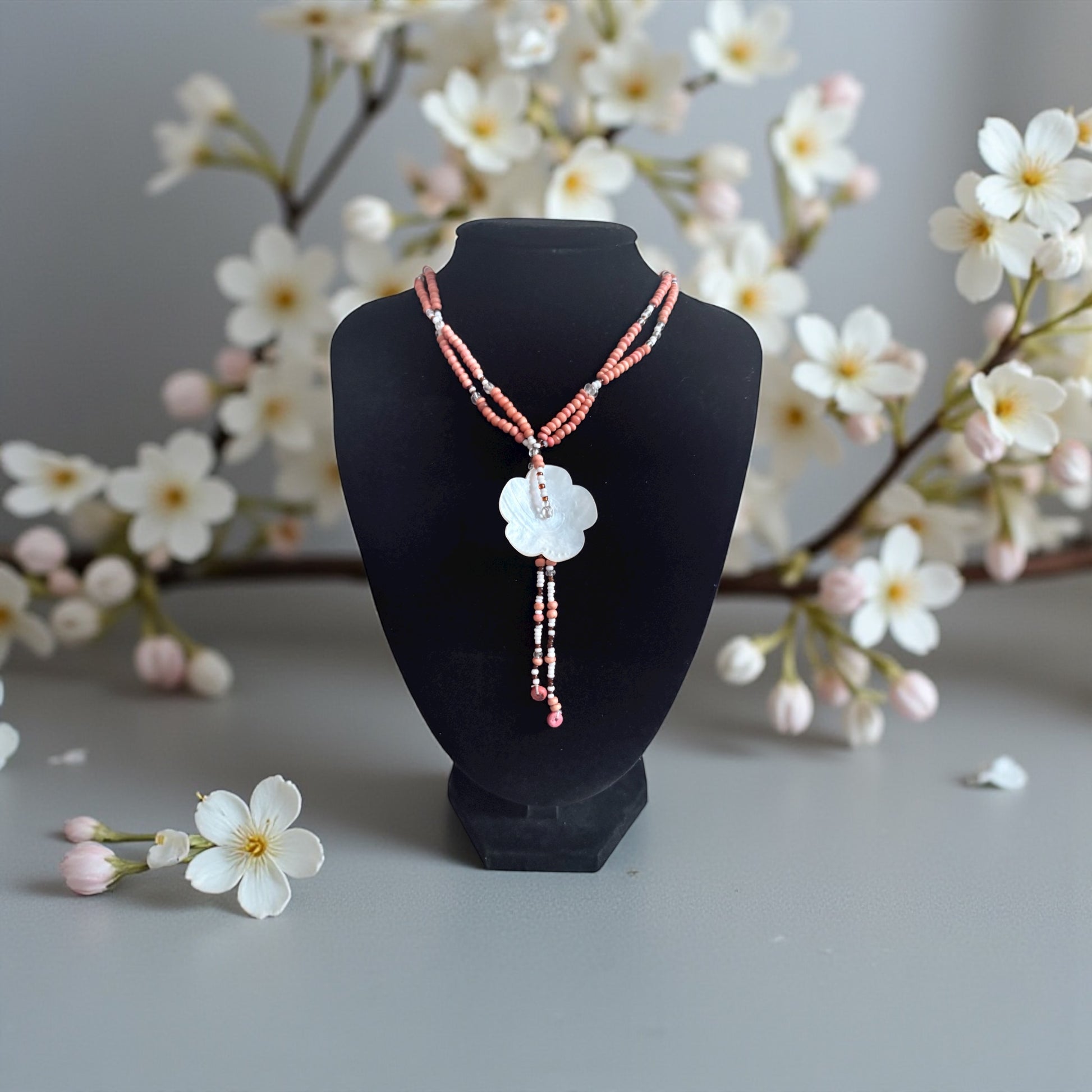 Necklace on a black mannequin bust with cherry blossom branches in the background