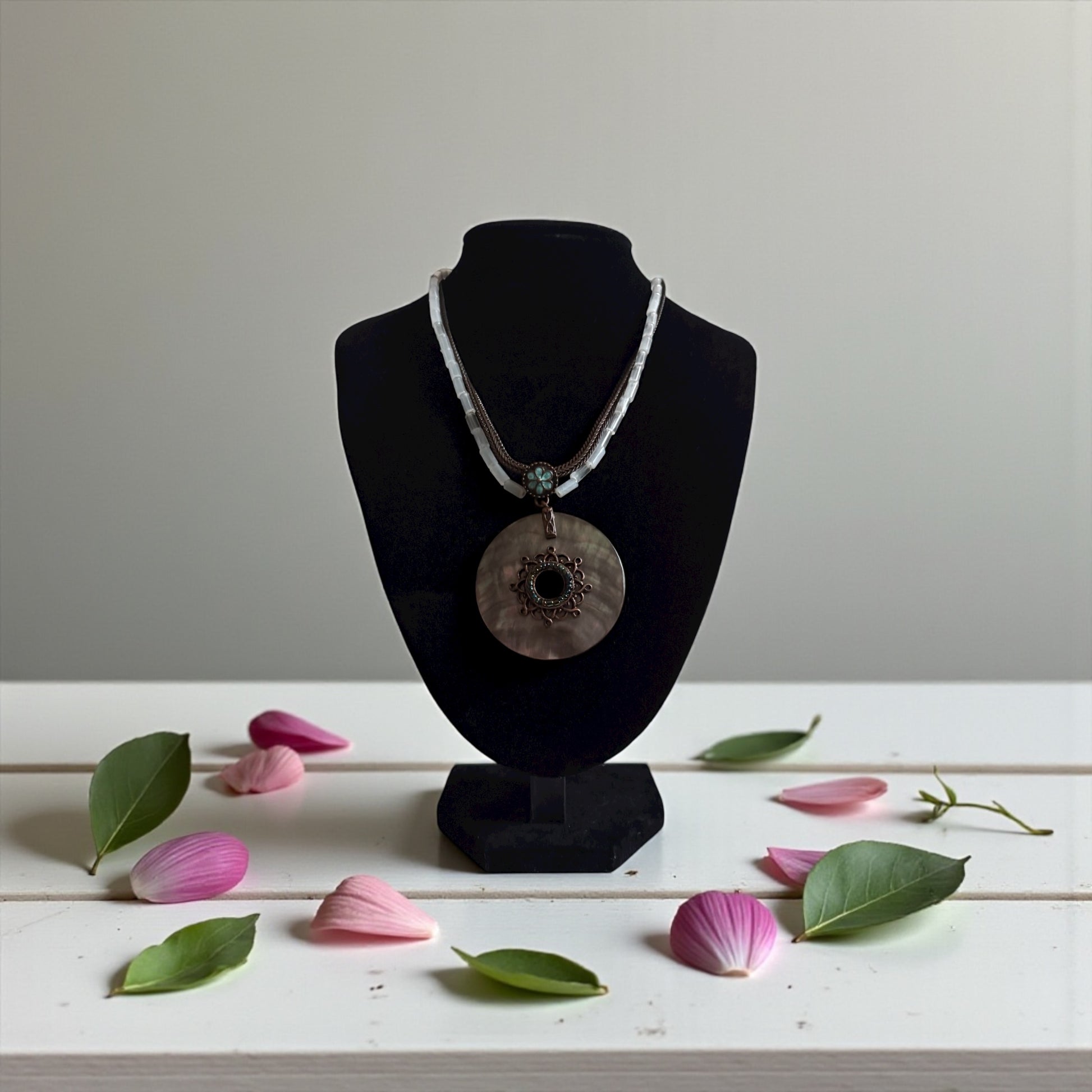 Necklace on a black mannequin bust with pink petals and green leaves on a white surface