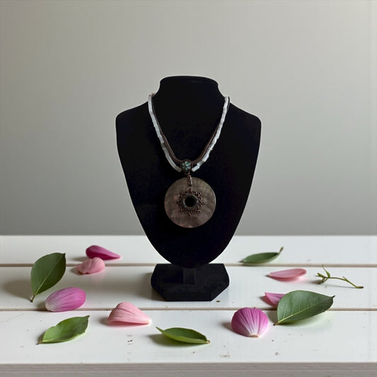 Necklace on a black mannequin bust with pink petals and green leaves on a white surface