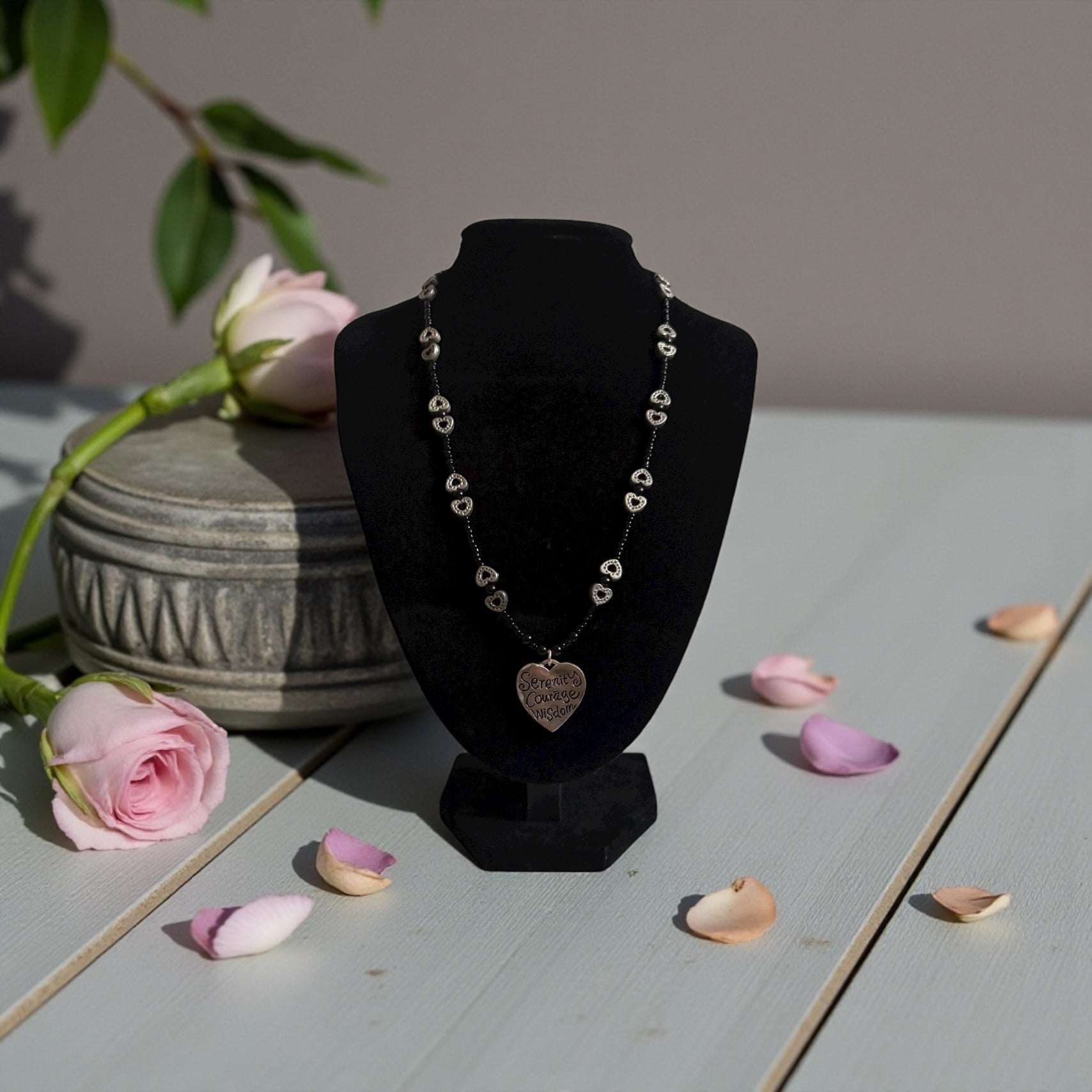 Necklace on a black bust with pink roses and petals on a light surface