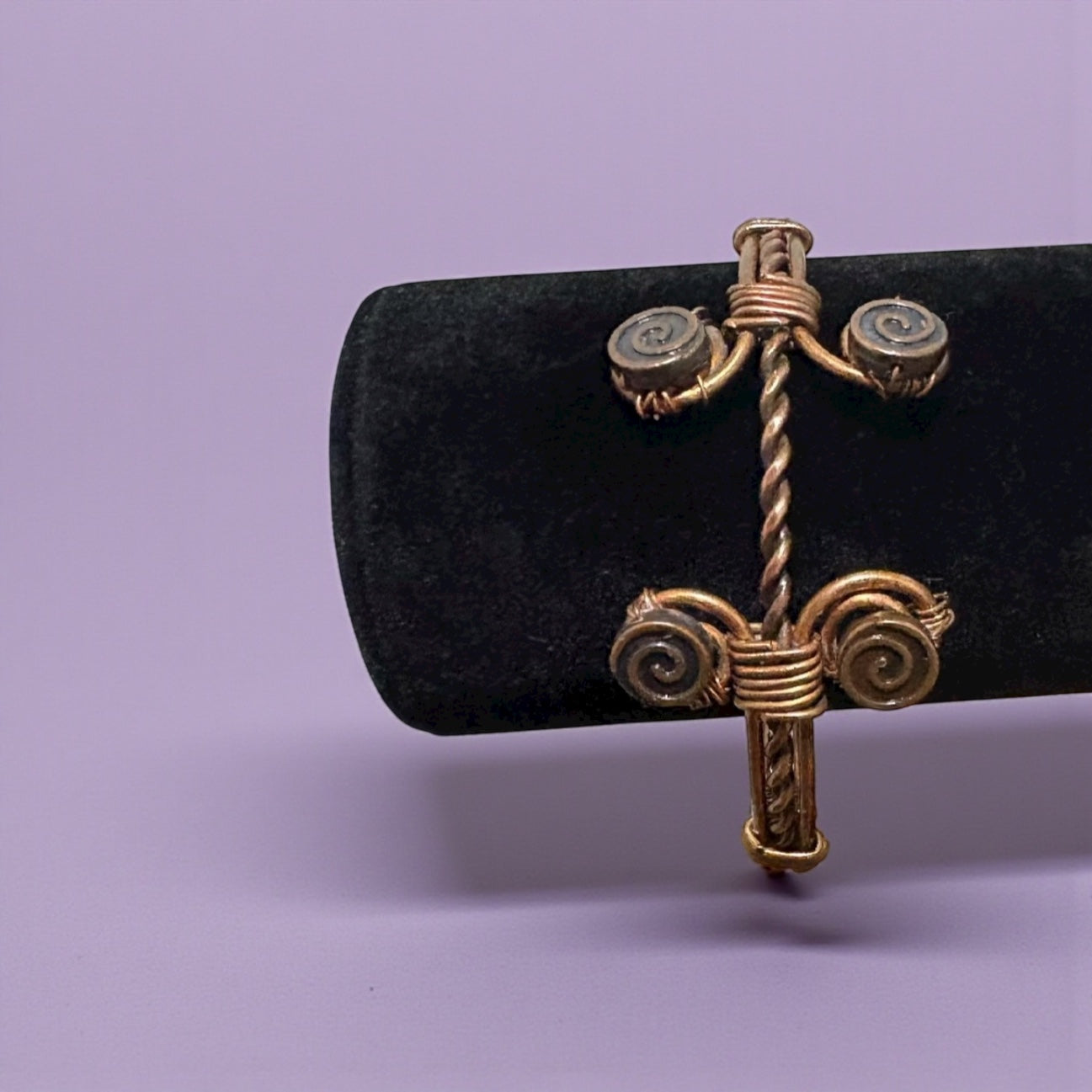 Gold cross-shaped earring on a black cushion against a purple background