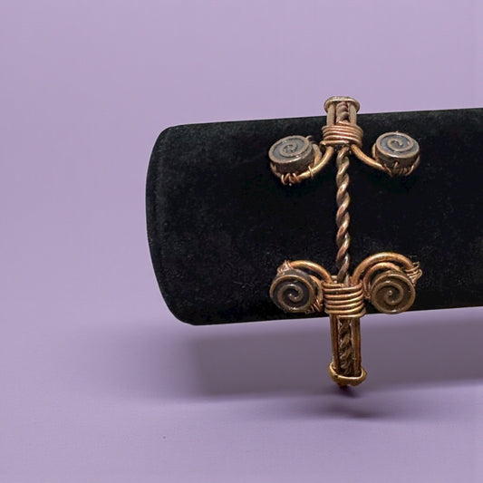 Gold cross-shaped earring on a black cushion against a purple background