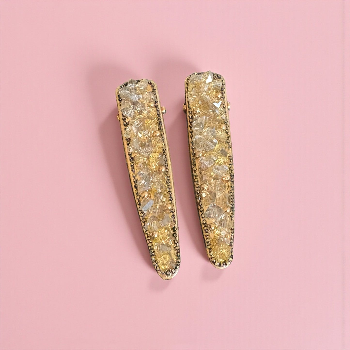 Gold bar earrings with a textured design on a pink background