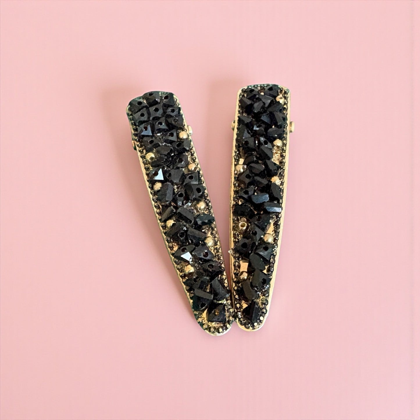 Black and gold hair clips on a pink background
