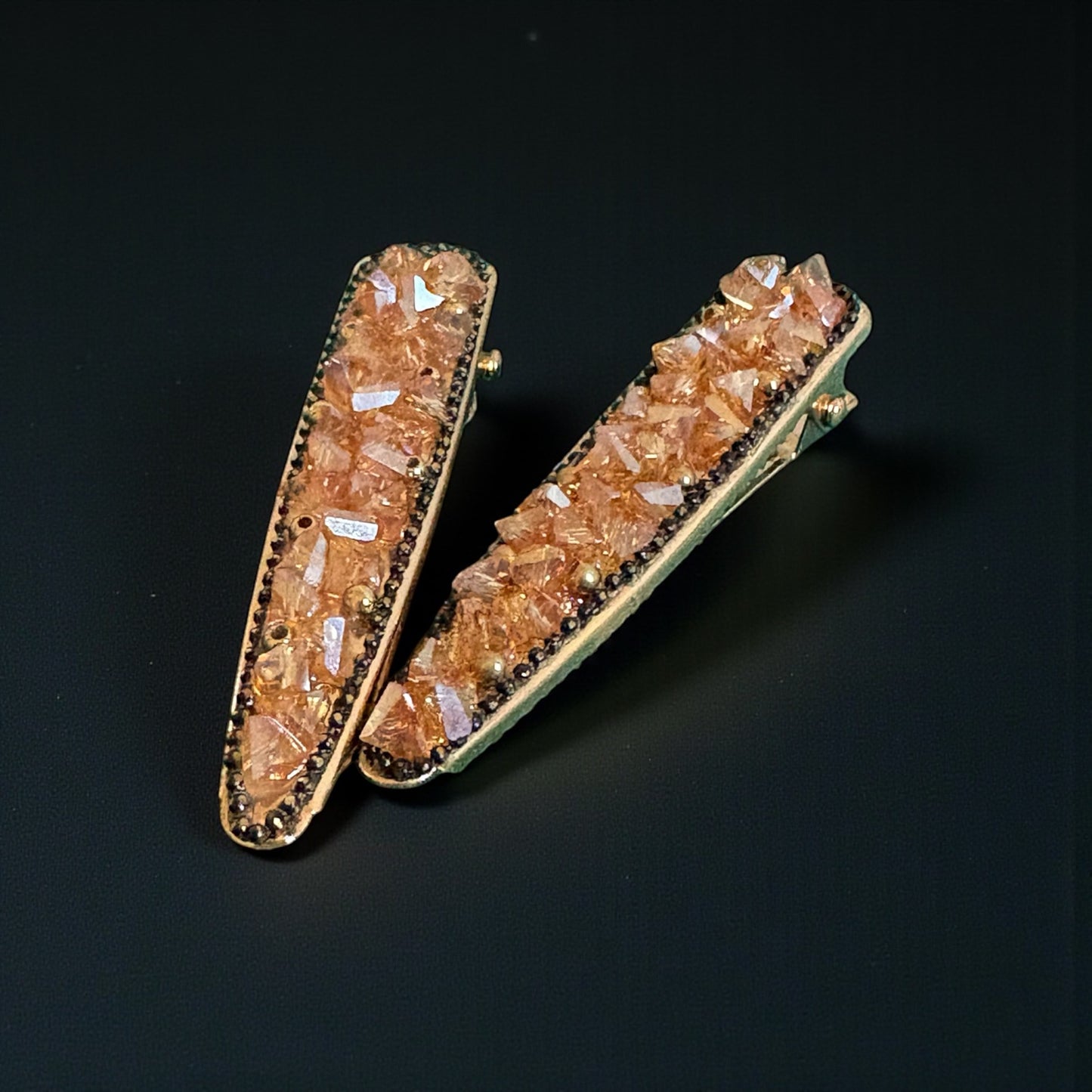 Two decorative hair clips with crystal-like stones on a black background