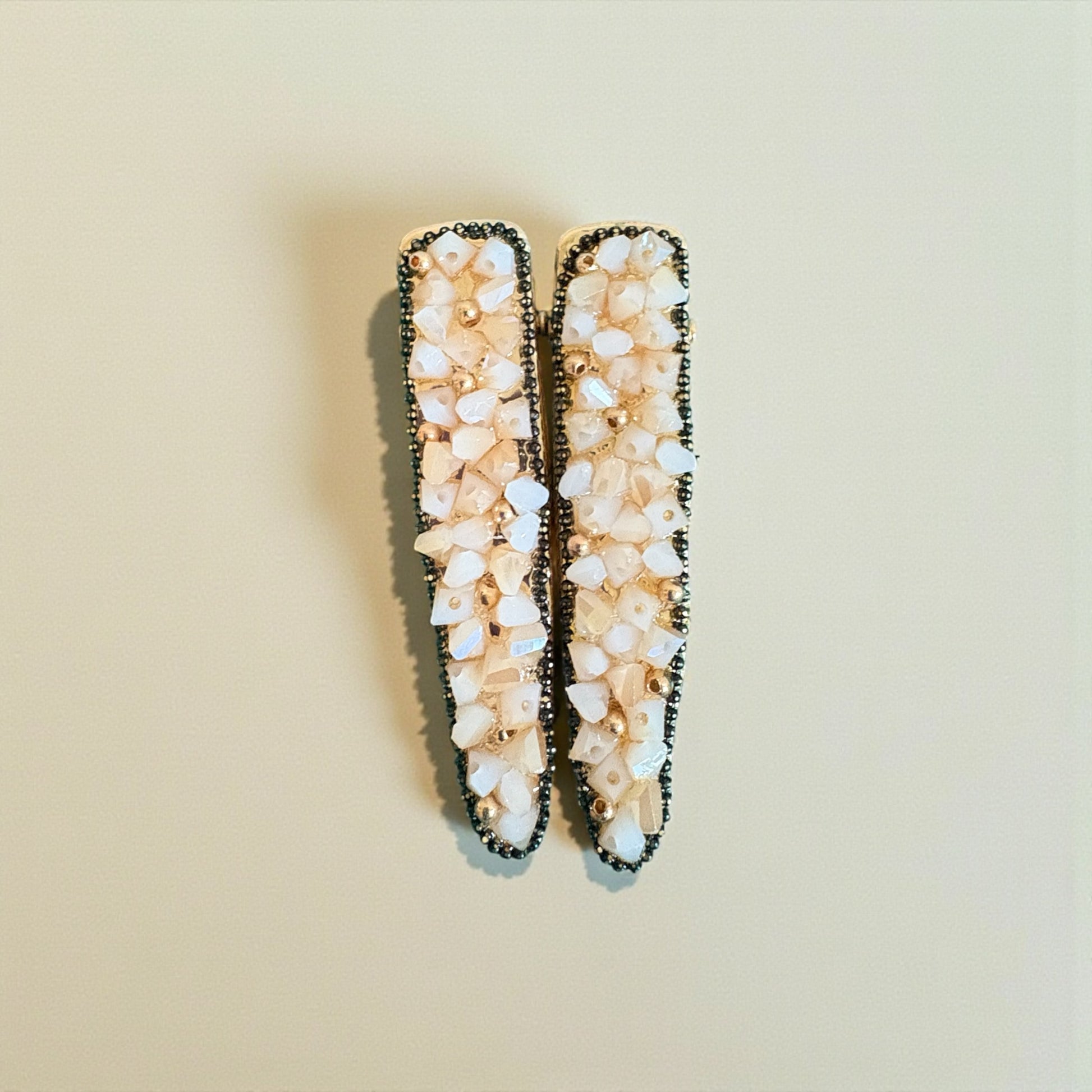 Pair of decorative hair clips with beige stones on a beige background