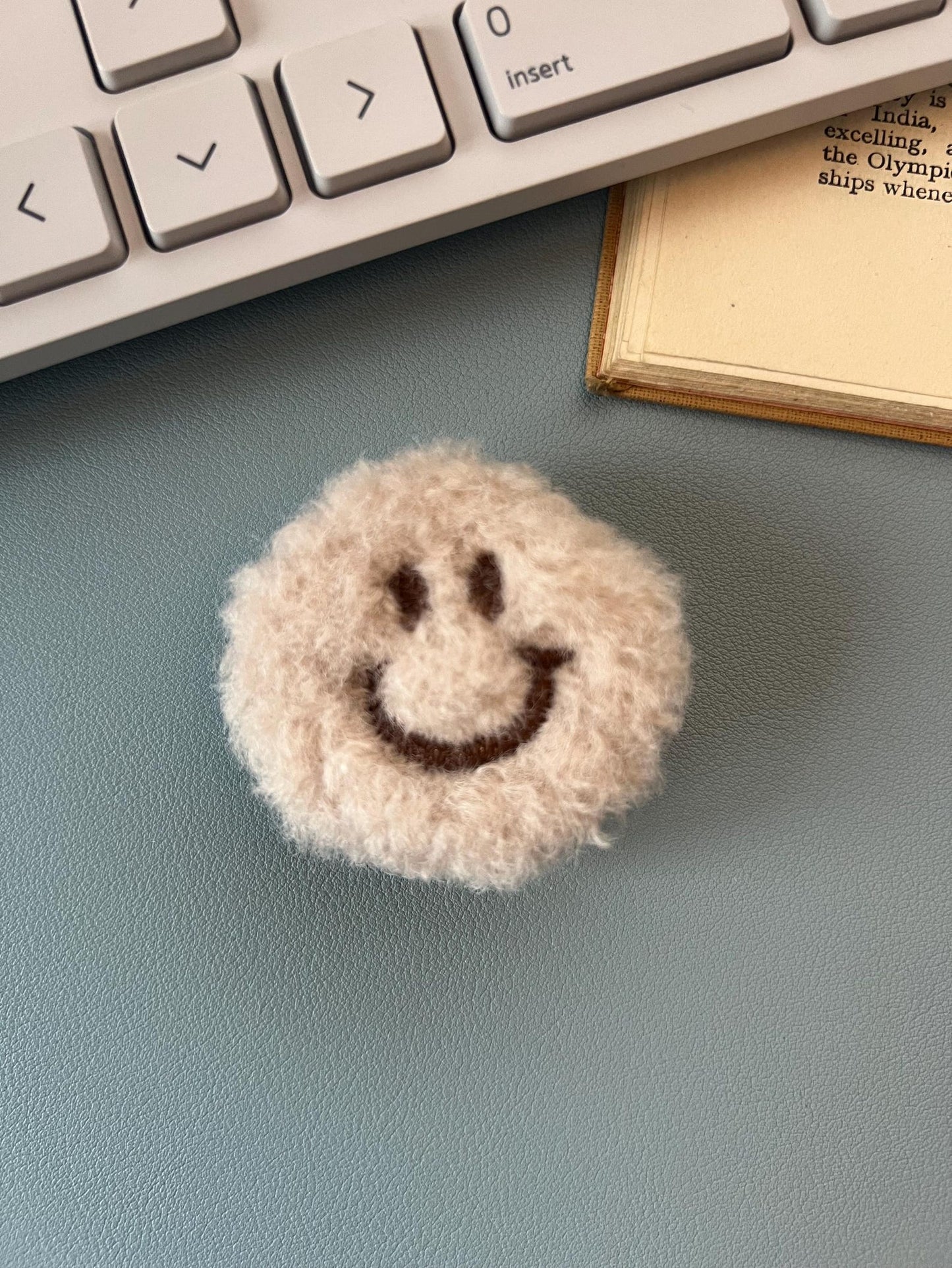 Smiley face plush phone grip on a desk next to a keyboard