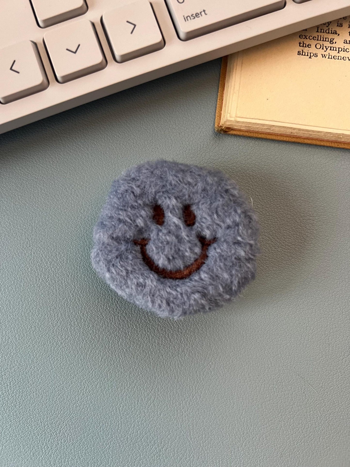 Round gray object with a smiley face on a desk next to a keyboard and book