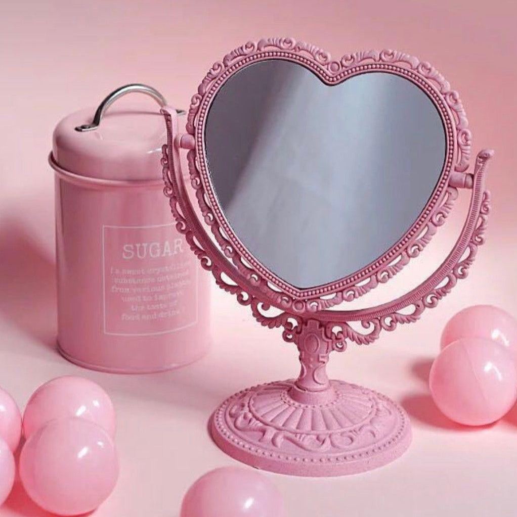 Pink heart-shaped mirror with a pink container and balloons on a pink background