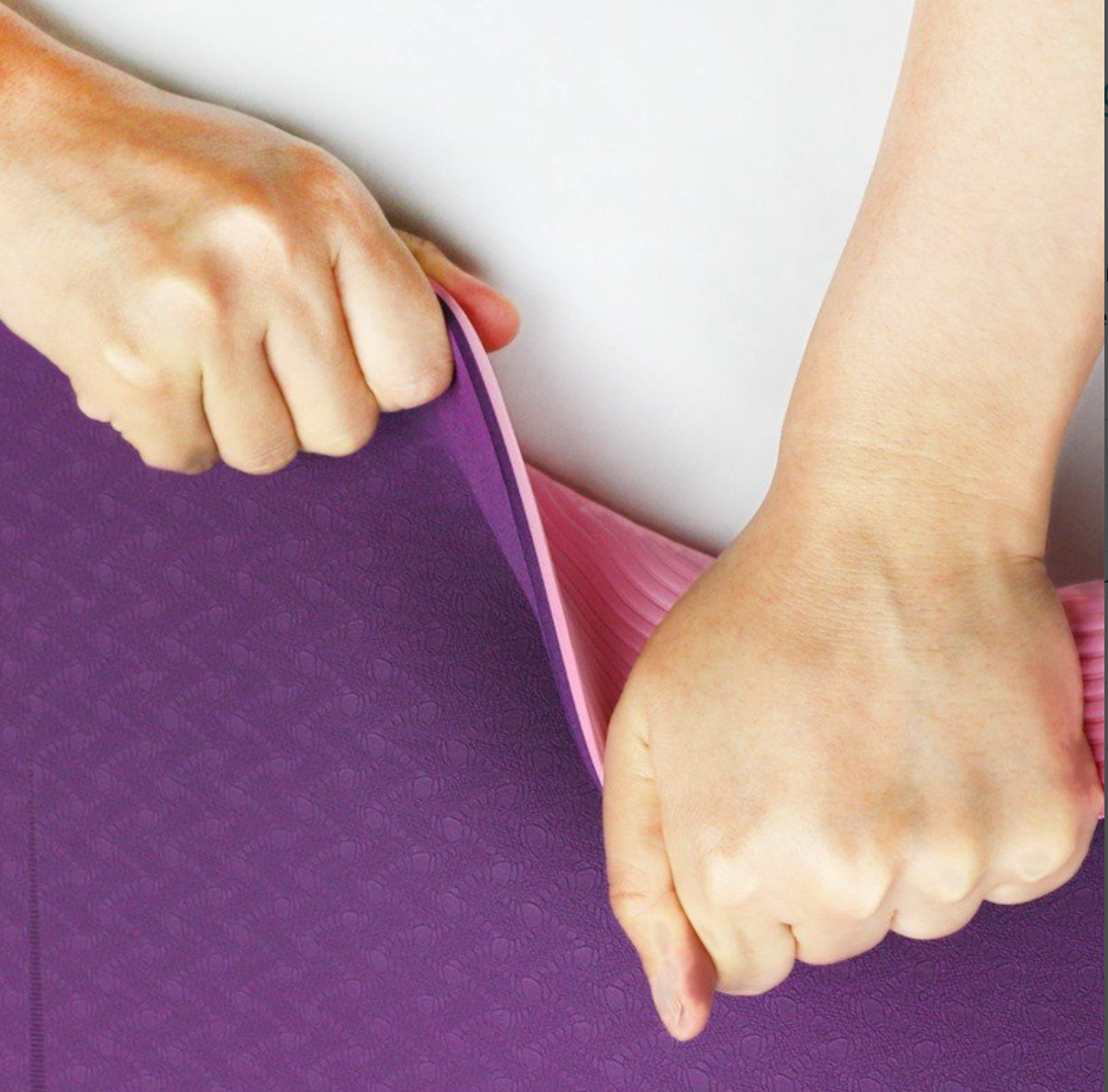 Purple yoga mat with pink border held by two hands against a white background