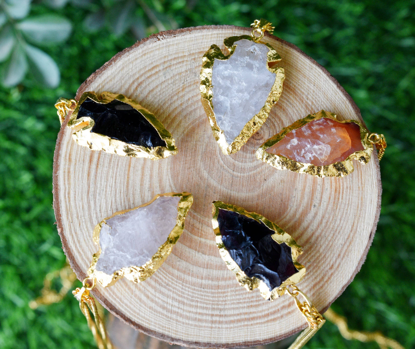 Gold-framed gemstone earrings on a wooden block with a green grass background